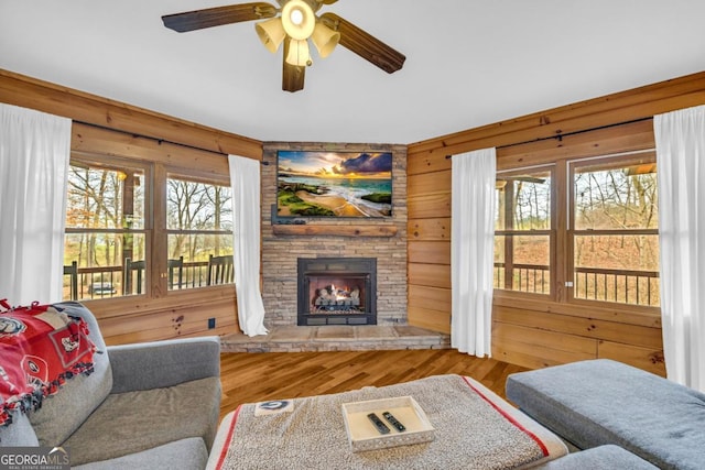 living room with hardwood / wood-style floors, a stone fireplace, wooden walls, and ceiling fan