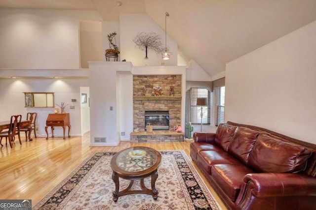 living room featuring high vaulted ceiling, a stone fireplace, and light hardwood / wood-style floors