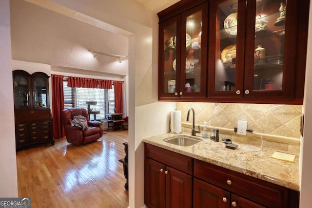 bar featuring tasteful backsplash, sink, light stone counters, and light wood-type flooring