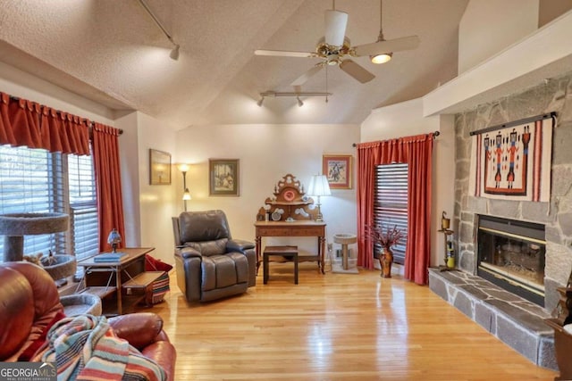 living room featuring vaulted ceiling, a stone fireplace, wood-type flooring, ceiling fan, and a textured ceiling