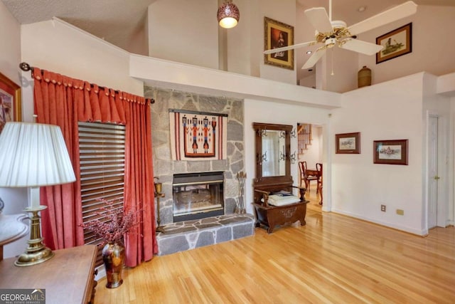 living room with hardwood / wood-style floors, a fireplace, ceiling fan, and a high ceiling