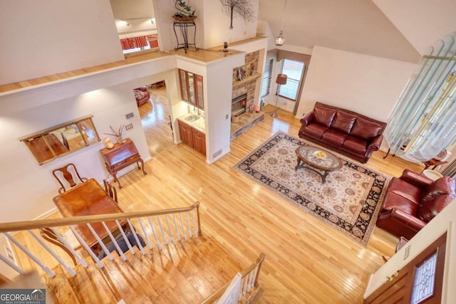 living room with hardwood / wood-style flooring, a stone fireplace, and high vaulted ceiling