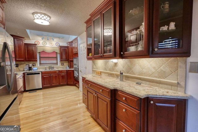 kitchen featuring appliances with stainless steel finishes, tasteful backsplash, sink, a textured ceiling, and light hardwood / wood-style flooring