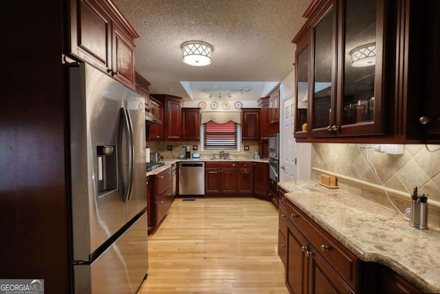 kitchen featuring appliances with stainless steel finishes, tasteful backsplash, light stone counters, a textured ceiling, and light hardwood / wood-style flooring