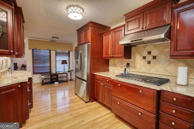 kitchen with light hardwood / wood-style flooring, backsplash, stainless steel appliances, light stone countertops, and a textured ceiling