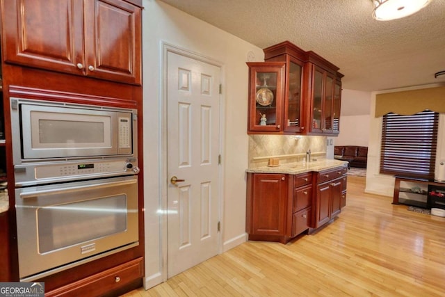 kitchen with a textured ceiling, appliances with stainless steel finishes, light stone countertops, light hardwood / wood-style floors, and backsplash