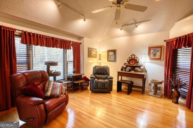 living area featuring lofted ceiling, ceiling fan, hardwood / wood-style flooring, and a textured ceiling