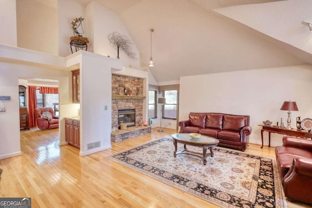 living room with a stone fireplace, light hardwood / wood-style flooring, and high vaulted ceiling