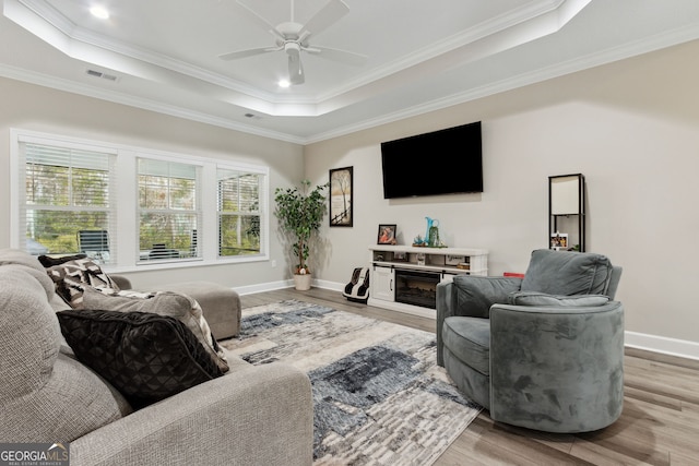 living room with ceiling fan, ornamental molding, a raised ceiling, and hardwood / wood-style floors