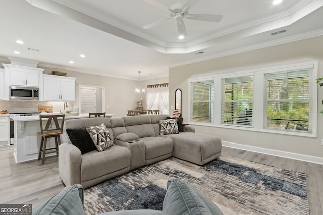 living room featuring ceiling fan with notable chandelier, ornamental molding, a tray ceiling, and light hardwood / wood-style floors