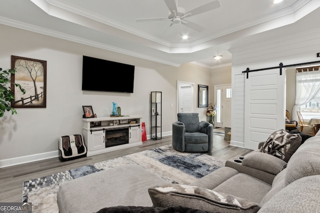 living room featuring a raised ceiling, ornamental molding, a barn door, and dark hardwood / wood-style floors