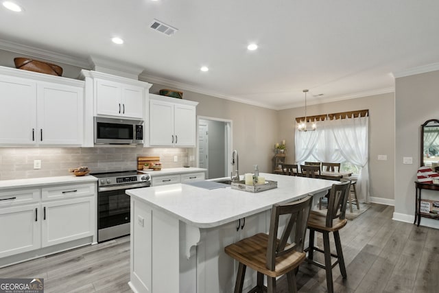 kitchen featuring white cabinetry, hanging light fixtures, a kitchen island with sink, and stainless steel appliances