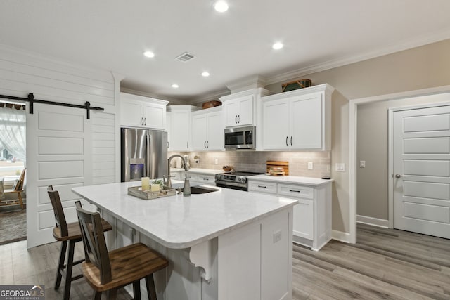 kitchen with stainless steel appliances, a barn door, a center island with sink, and white cabinets