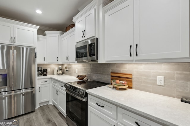 kitchen with crown molding, appliances with stainless steel finishes, white cabinetry, tasteful backsplash, and light wood-type flooring