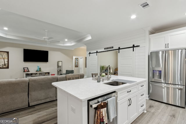 kitchen featuring white cabinetry, a kitchen island with sink, stainless steel appliances, a tray ceiling, and a barn door