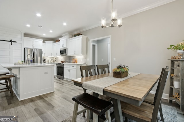 dining area featuring sink, an inviting chandelier, light hardwood / wood-style flooring, ornamental molding, and a barn door