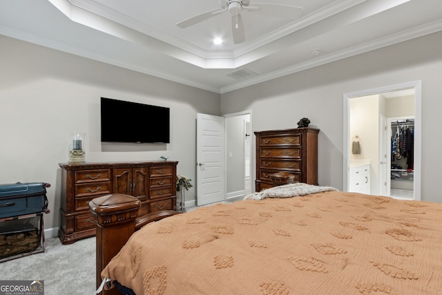 carpeted bedroom with ensuite bathroom, a spacious closet, ornamental molding, a tray ceiling, and ceiling fan