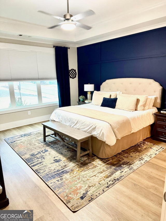 bedroom with a raised ceiling, hardwood / wood-style floors, and ceiling fan