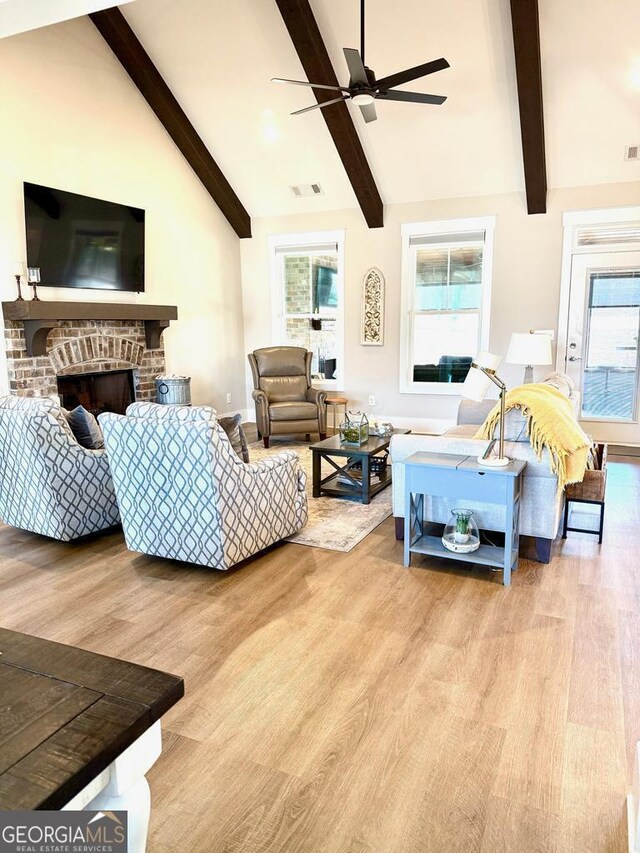 living room featuring a brick fireplace, light hardwood / wood-style flooring, lofted ceiling with beams, and ceiling fan