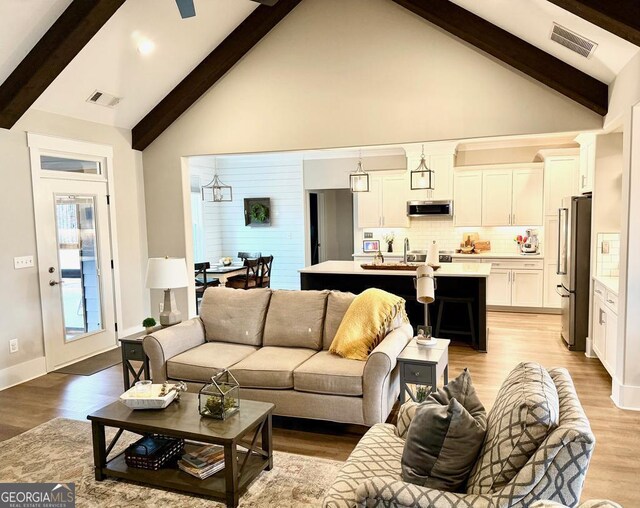 living room with high vaulted ceiling, beamed ceiling, and light wood-type flooring