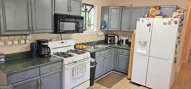 190 Creekwood Rd, Winder, GA 30680 - kitchen featuring dark countertops, gray cabinetry, a sink, light wood finished floors, and white appliances