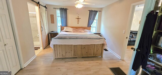 190 Creekwood Rd, Winder, GA 30680 - bedroom with a barn door, ensuite bath, light wood-style flooring, baseboards, and visible vents