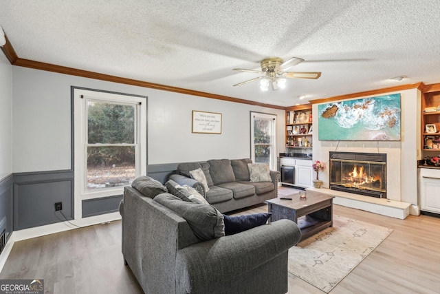 living room featuring ornamental molding, light wood-type flooring, built in features, and a textured ceiling