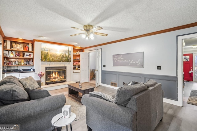 living room featuring built in shelves, wood-type flooring, ornamental molding, and a textured ceiling