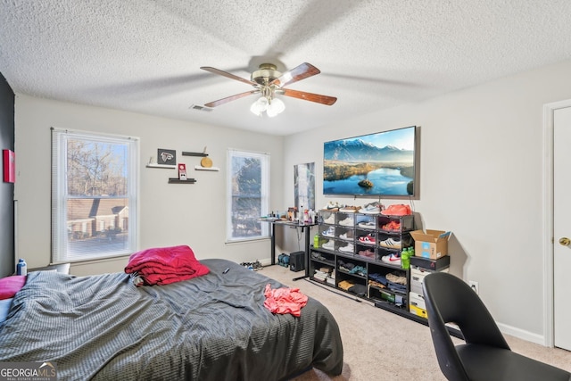 bedroom with ceiling fan, light colored carpet, and a textured ceiling