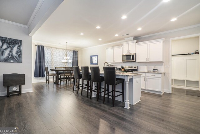 kitchen with a breakfast bar area, appliances with stainless steel finishes, white cabinetry, an island with sink, and light stone countertops