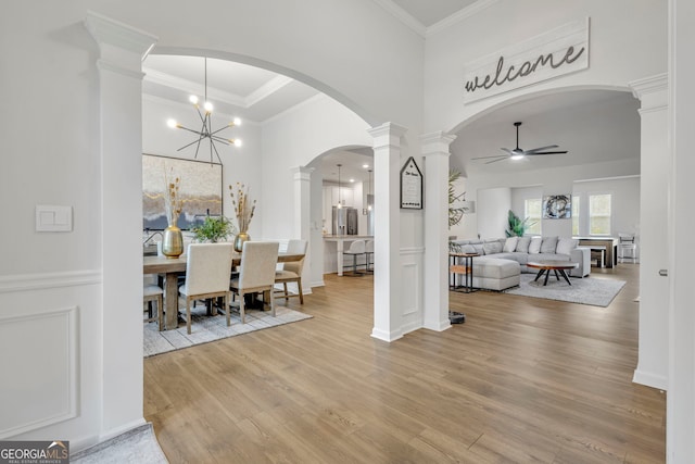 dining area featuring a high ceiling, ornamental molding, light hardwood / wood-style floors, ceiling fan with notable chandelier, and ornate columns