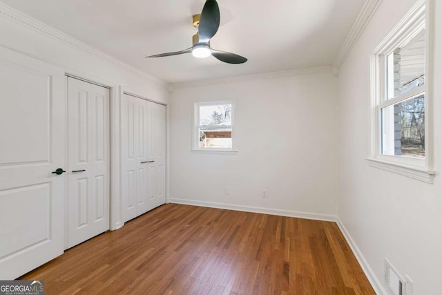 unfurnished bedroom featuring two closets, ornamental molding, ceiling fan, and hardwood / wood-style flooring