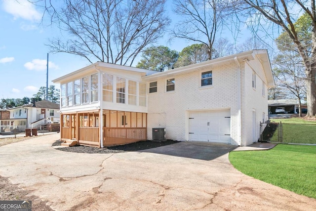 exterior space featuring a garage, a sunroom, central air condition unit, and a lawn