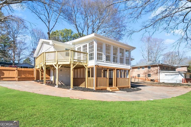 rear view of property featuring a sunroom, a deck, and a lawn