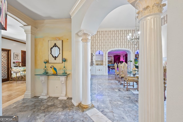 hall featuring a notable chandelier, ornamental molding, and ornate columns