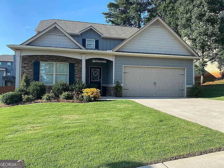 craftsman house with a front lawn, driveway, a garage, stone siding, and board and batten siding