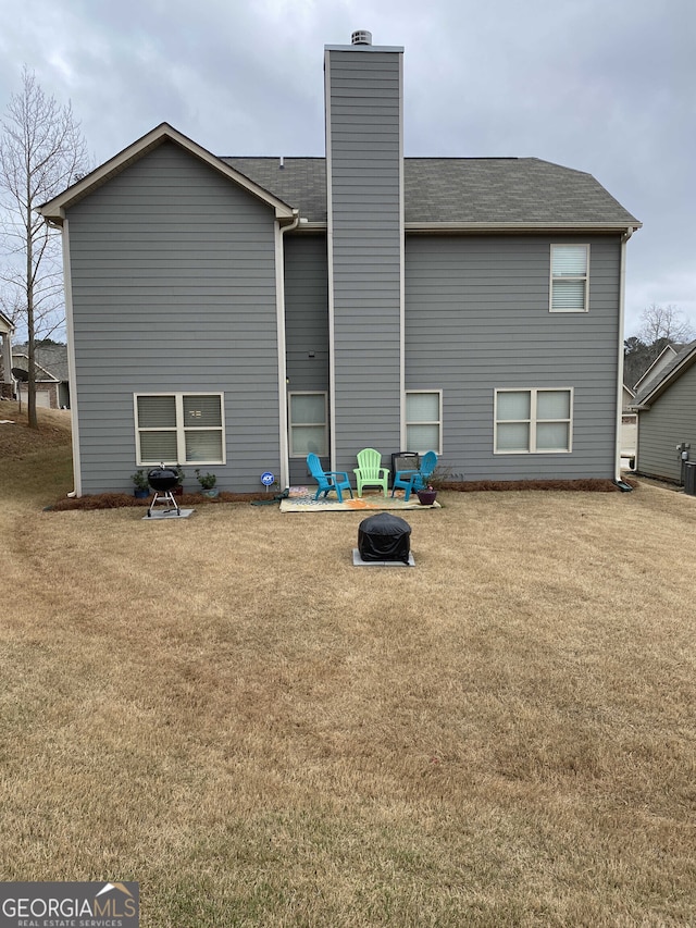 back of house with a fire pit, a lawn, roof with shingles, and a chimney