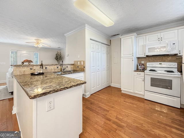 kitchen featuring white appliances, white cabinetry, a sink, and a peninsula