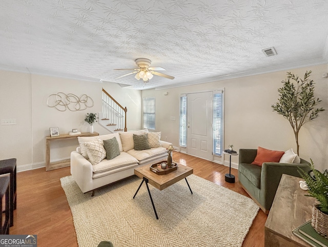 living room with crown molding, visible vents, wood finished floors, baseboards, and stairs