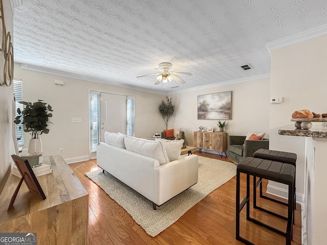 living area with crown molding, visible vents, a textured ceiling, wood finished floors, and baseboards