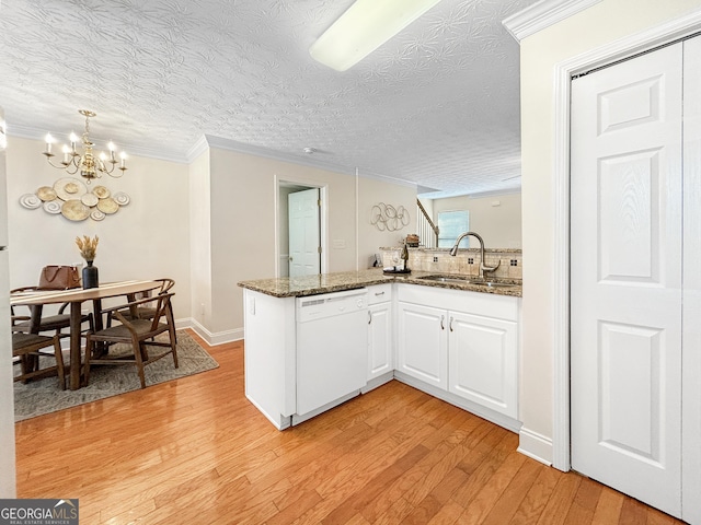 kitchen with white cabinetry, white dishwasher, a sink, dark stone countertops, and a peninsula