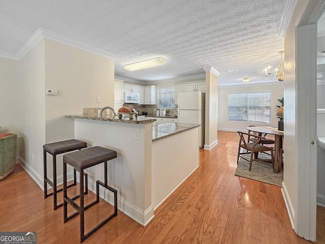 kitchen featuring light wood finished floors, white cabinets, dark stone countertops, white appliances, and a peninsula