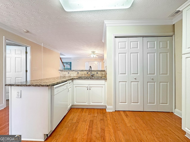 kitchen with a peninsula, a sink, white cabinetry, dishwasher, and dark stone countertops