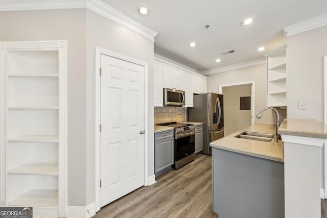 kitchen with appliances with stainless steel finishes, sink, white cabinets, ornamental molding, and kitchen peninsula