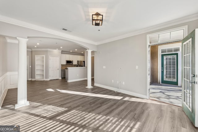 unfurnished living room featuring decorative columns, ornamental molding, and hardwood / wood-style floors