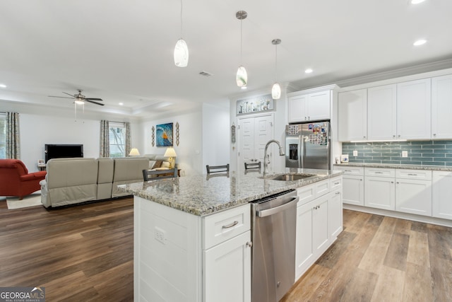 kitchen with hanging light fixtures, stainless steel appliances, an island with sink, white cabinets, and a raised ceiling