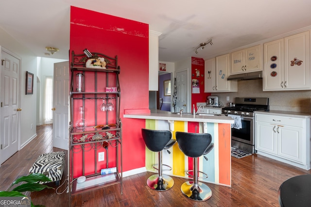 kitchen featuring dark hardwood / wood-style floors, white cabinets, a kitchen bar, kitchen peninsula, and stainless steel gas range