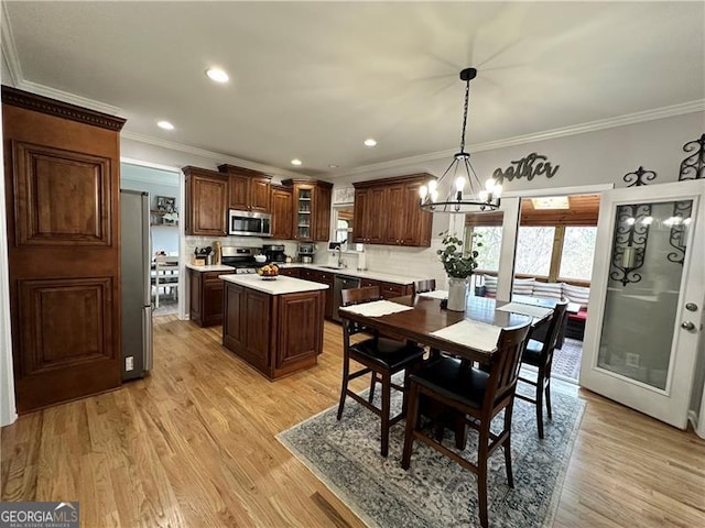 dining area featuring an inviting chandelier, ornamental molding, sink, and light hardwood / wood-style flooring