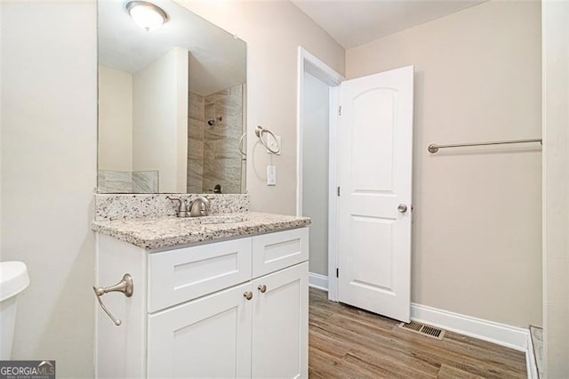 bathroom featuring vanity, tiled shower, hardwood / wood-style floors, and toilet