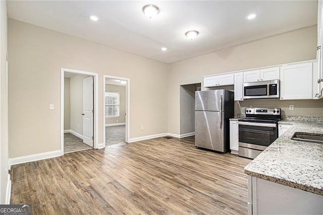 kitchen with white cabinetry, appliances with stainless steel finishes, light stone counters, and light hardwood / wood-style floors